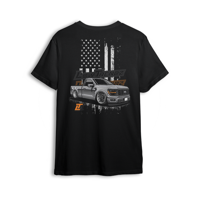 T-shirt featuring a slammed, murdered-out single cab Ford F-150 in front of a distressed American flag with burnt orange Low Trendz branding. The Stars, Stripes & Stance t-shirt delivers bold Ford energy and custom street presence for true lifestyle reps.
