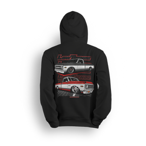 Hoodie featuring two slammed Chevy C10s—one silver, one red and white two-tone—laid out over a grid floor with a layered Low Trendz backdrop. The Two-Tone Royalty hoodie blends vintage muscle with custom show truck style for builders who keep it classic, not basic.