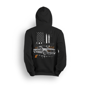 Hoodie featuring a slammed, murdered-out single cab Ford F-150 in front of a distressed American flag with burnt orange Low Trendz branding. The Stars, Stripes & Stance hoodie delivers bold Ford energy and custom street presence for true lifestyle reps.