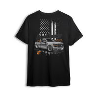 T-shirt featuring a slammed, murdered-out single cab Ford F-150 in front of a distressed American flag with burnt orange Low Trendz branding. The Stars, Stripes & Stance t-shirt delivers bold Ford energy and custom street presence for true lifestyle reps.